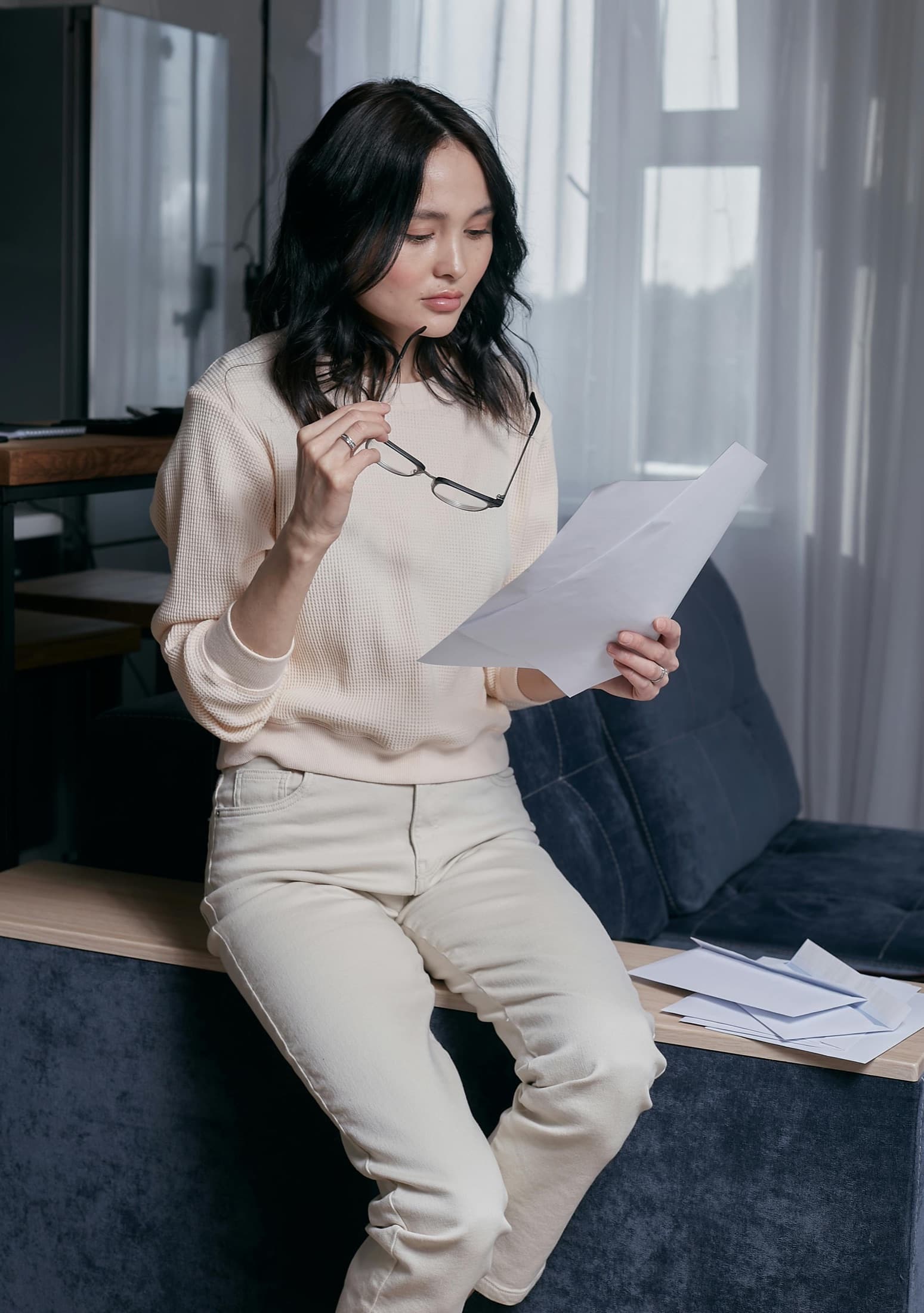 A woman reviewing paperwork, reading glasses in hand