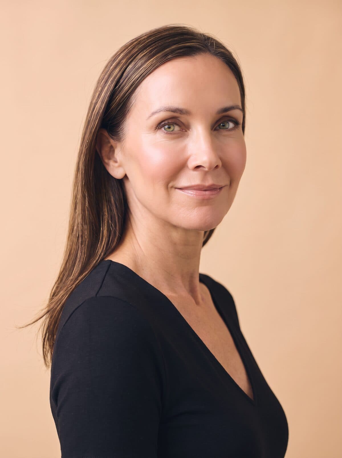 A woman with long hair in a black top, against a soft warm backdrop