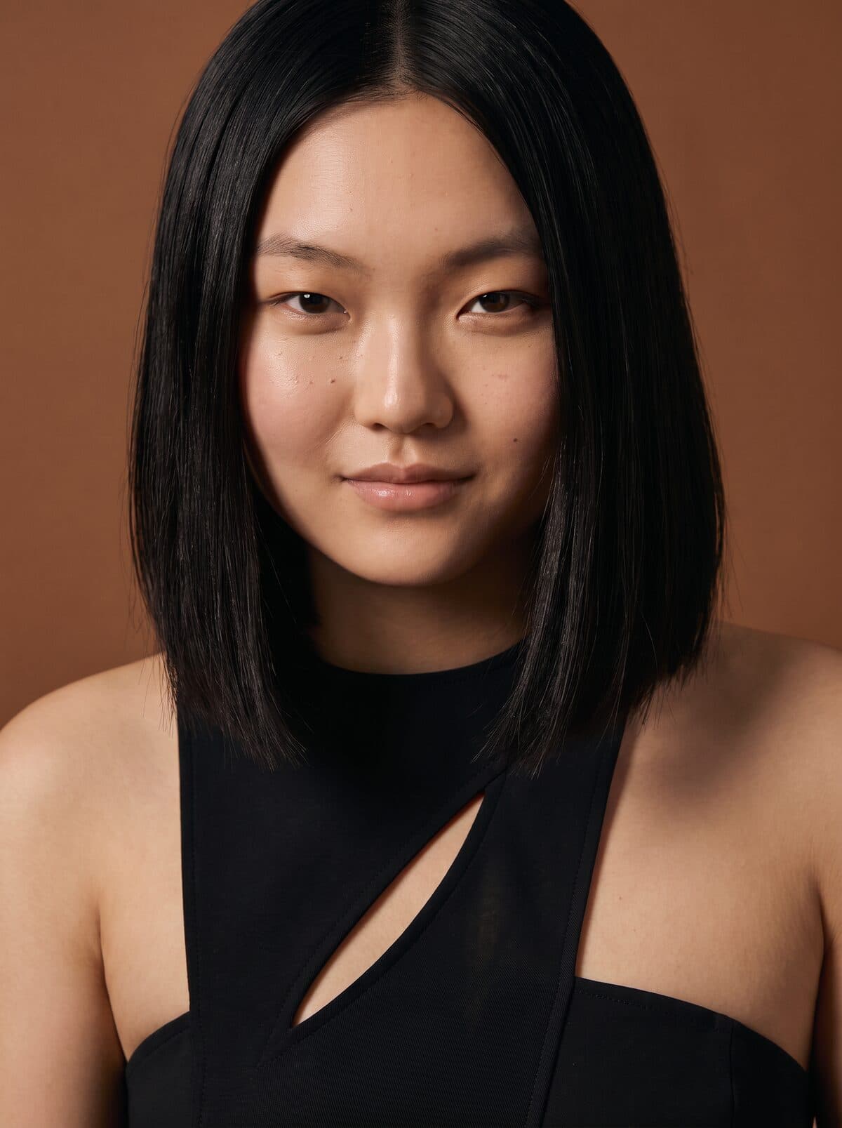 A woman with a dark bob, photographed against a warm terracotta backdrop