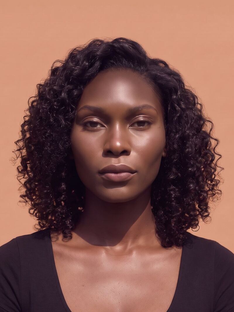 A woman with curly dark hair in a plum top, against a soft terracotta backdrop